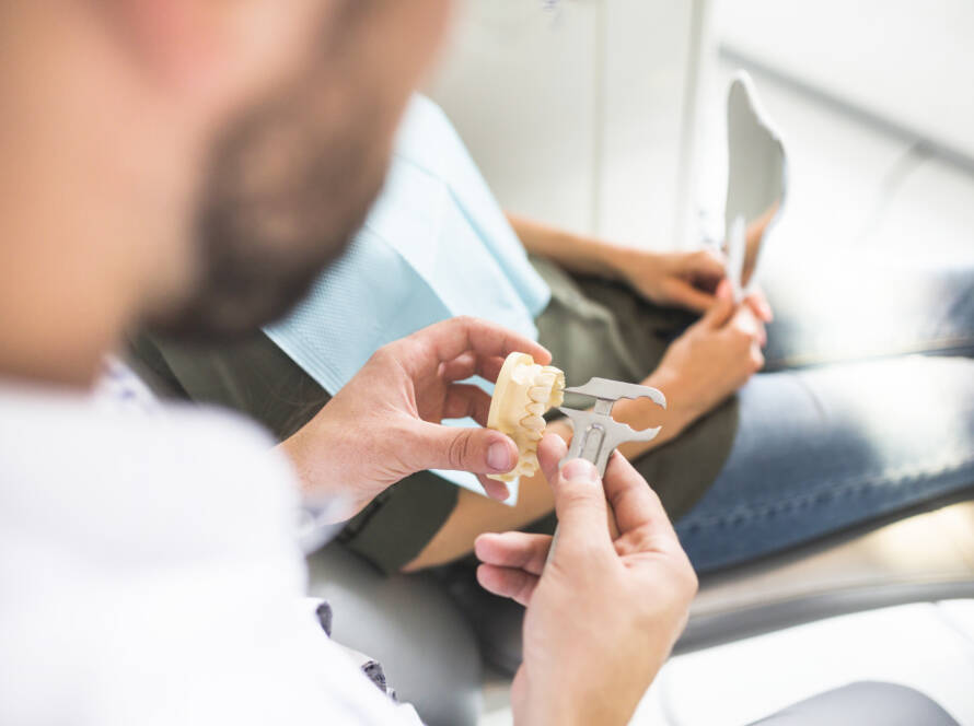 dentist-measuring-plastic-teeth-model-with-vernier-caliper